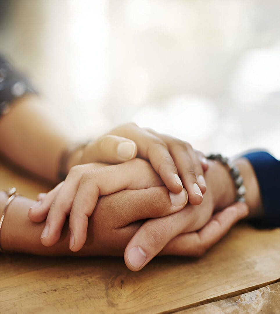 Hands clasped together on a wooden table.