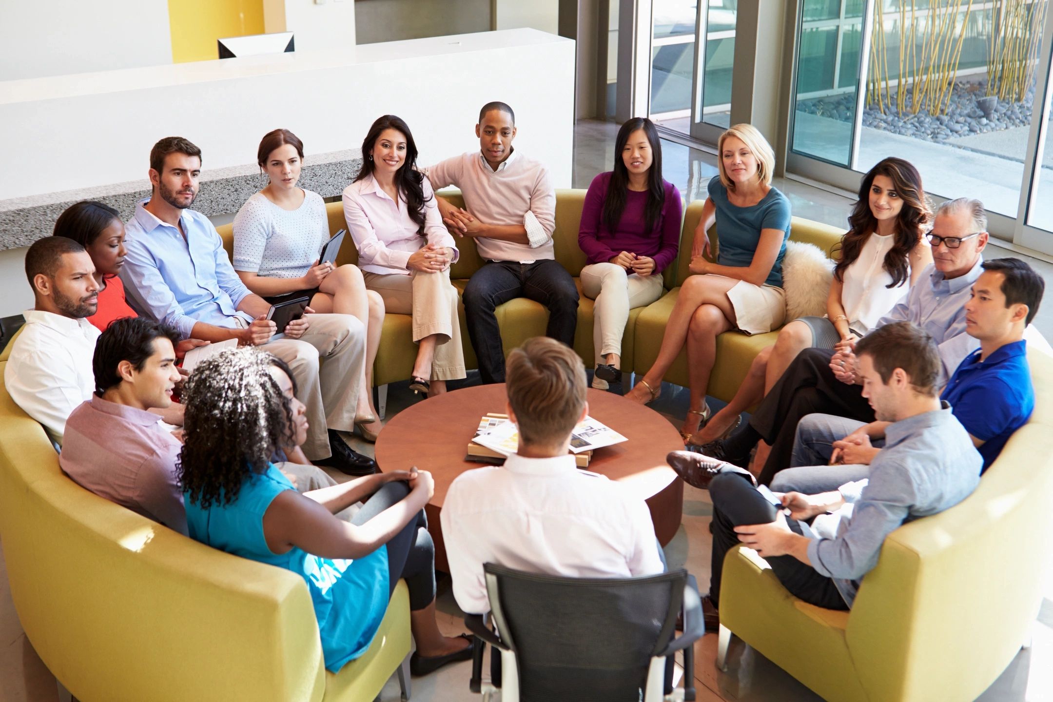 A diverse group in a meeting sitting in a circle in a bright room.